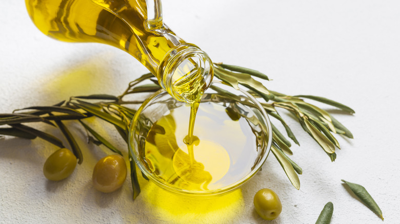 Bottle of olive oil pouring in bowl with olives