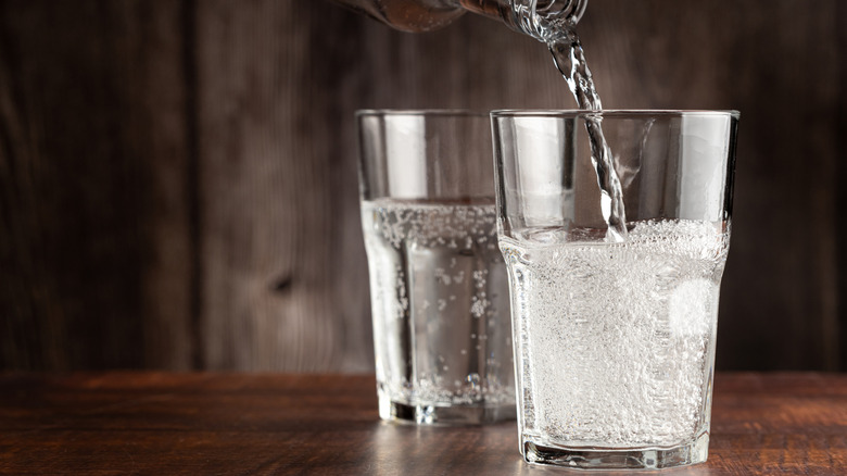 Seltzer water being poured into two glasses on dark brown wooden table