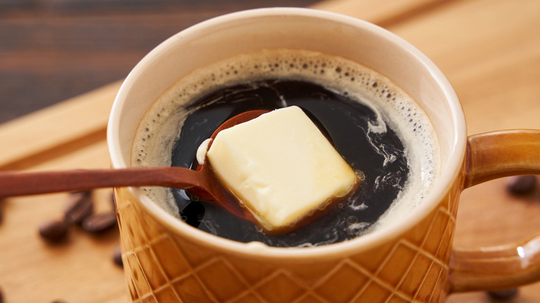 Close-up of pat of butter being spooned into cup of black coffee