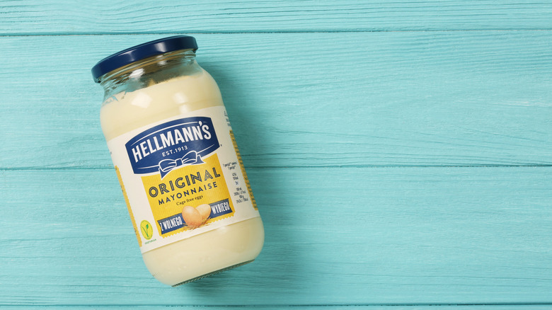 Glass jar of Hellmann's mayonnaise on blue, wood-grain background