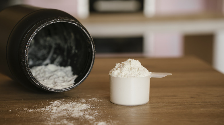 Scoop full of protein powder next to overturned container on wooden countertop