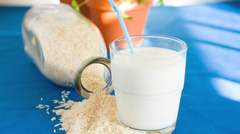 Glass of rice milk next to overturned glass jar with rice spilling out on blue tablecloth