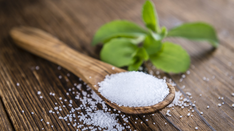 Wooden spoon of stevia granules on wooden table with stevia plant leaf