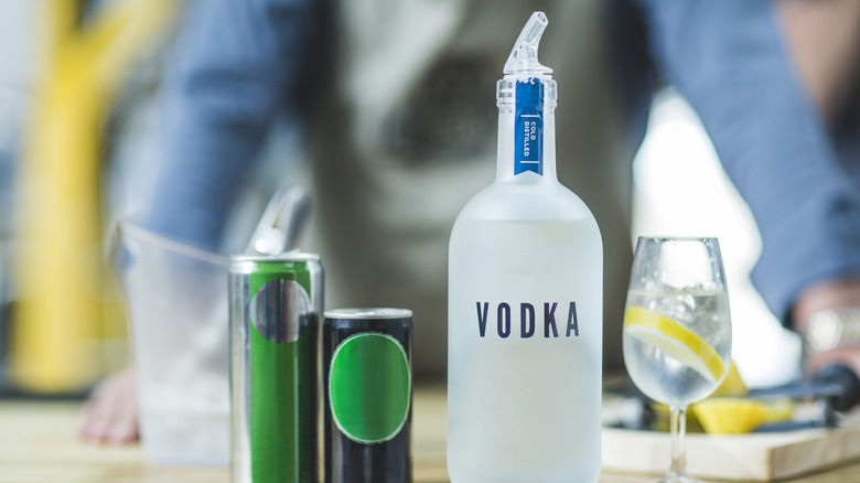 Unbranded vodka bottle on brightly-lit bar with cans and glass