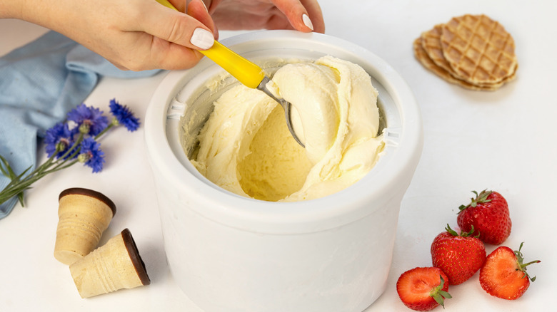 person scooping vanilla Ice cream from an ice cream maker drum