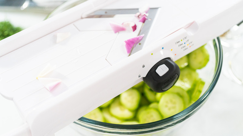 white plastic mandoline slicer over top of glass bowl of sliced cucumbers