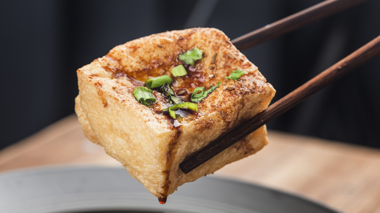 Chopsticks picking up fried tofu with scallion and sauce