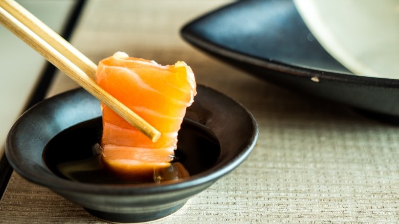 Chopsticks dipping salmon into shoyu