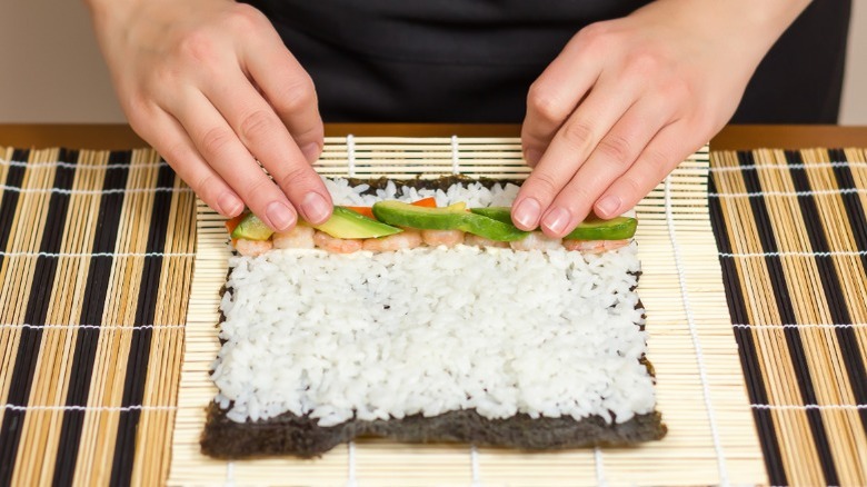 Hands rolling sushi with bamboo mat