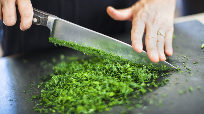 A person chopping fresh parsely with a large knife