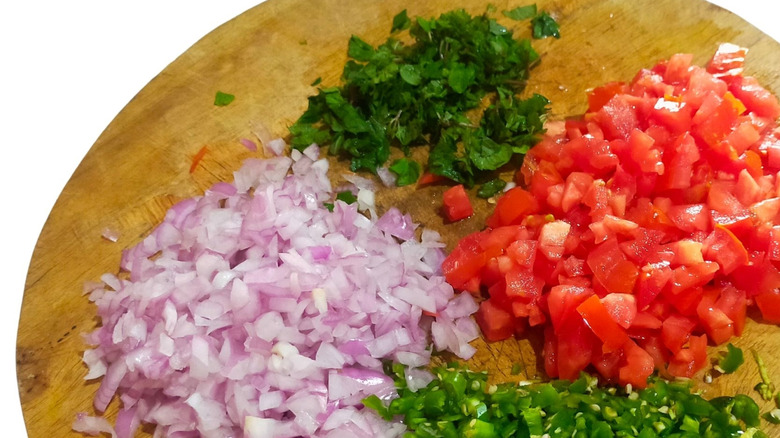 Chopped onions tomatoes and greens on a wooden board