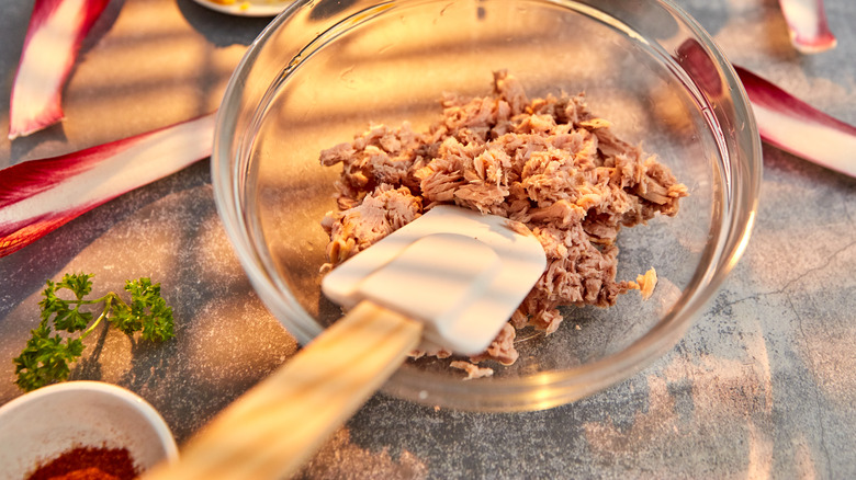 Tuna salad being prepared in a glass bowl with a spatula