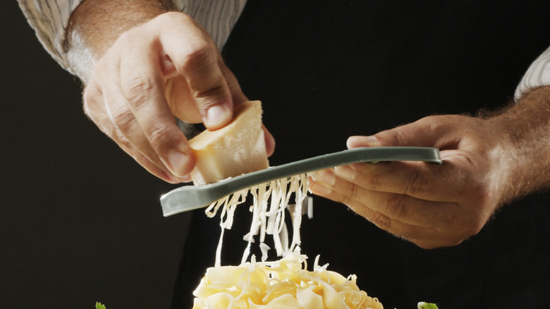 A person grates hard cheese on top of a freshly prepared pasta dish.