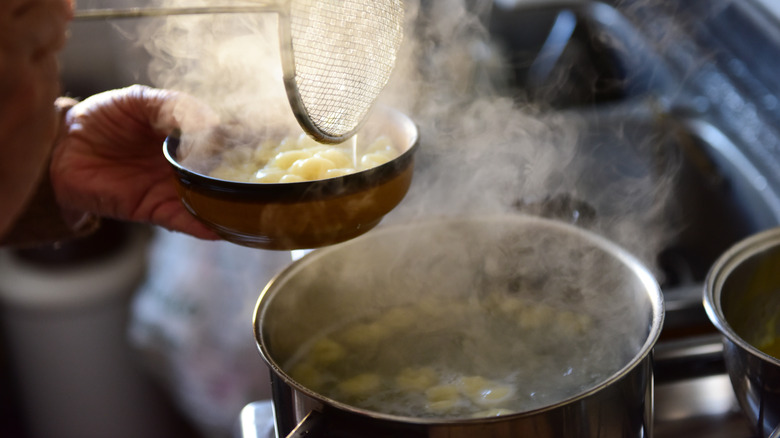 A person is straining home-made gnocchi out of a pot with boiling water using a steel colander into a bowl.