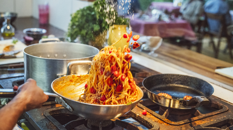 A person is tossing pasta in a pan over the stove.