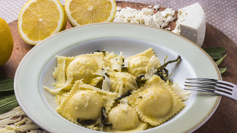 Ravioli sits in a bowl beside lemons and cheese.