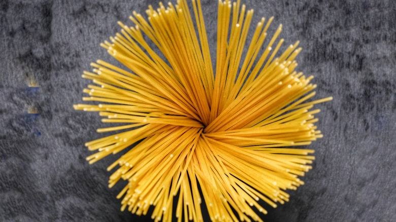 Uncooked spaghetti is arranged in a radius on a dark background of a slate board.