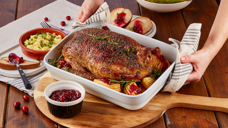 Hands holding white casserole dish with roasted duck