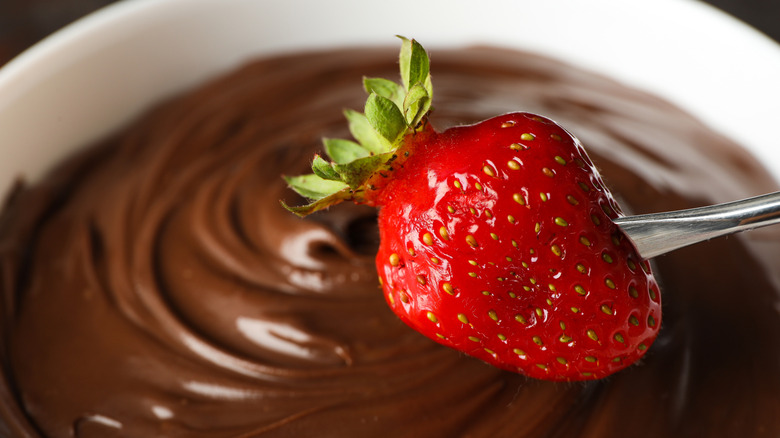 Delicious chocolate fondue dessert in a bowl with a strawberry about to be dipped into it