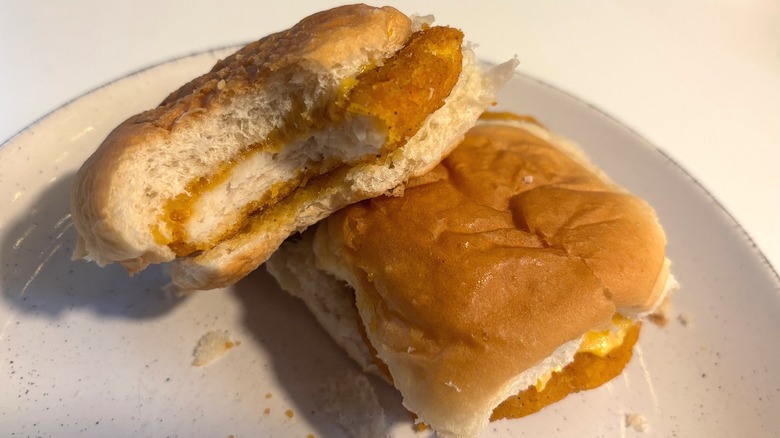 Two frozen White Castle chicken sliders on white plate, one with bite taken out of it