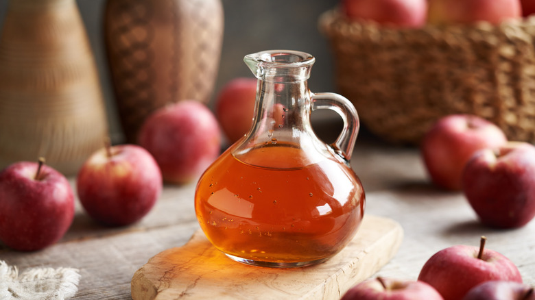 Apple cider vinegar on a cutting board with whole apples