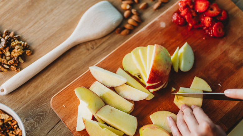 hands slicing apples on wooden cutting board