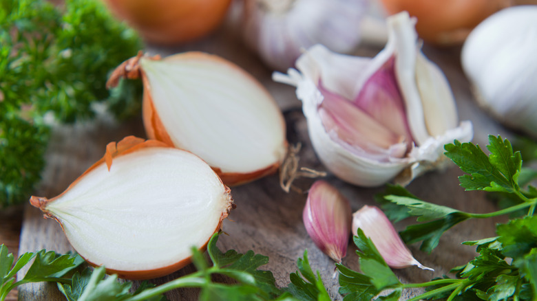 Onion, garlic, and herbs on wooden cutting board