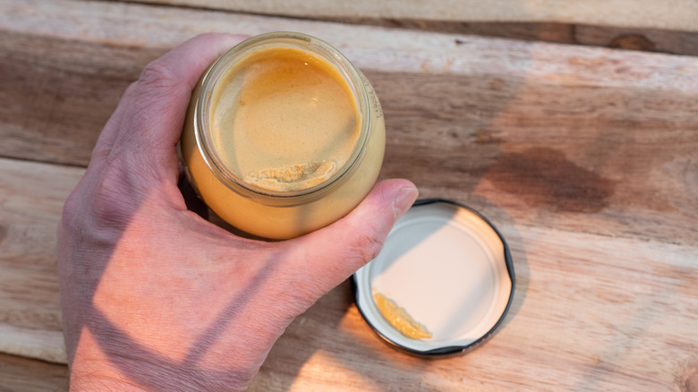 Hand holding opened jar of Dijon mustard