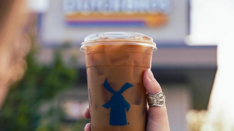 hand holding coffee drink in front of blurred Dutch Bros sign