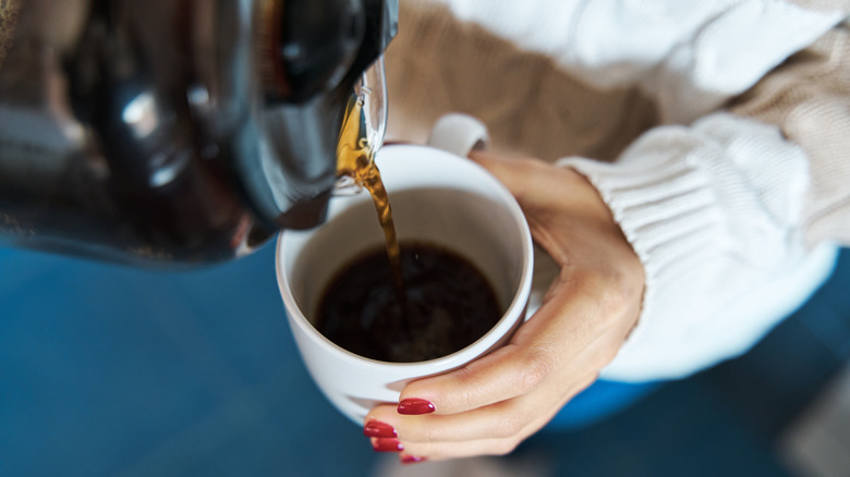 Close-up of woman's hands holding a cup of coffee, pouring into it from a coffee canister