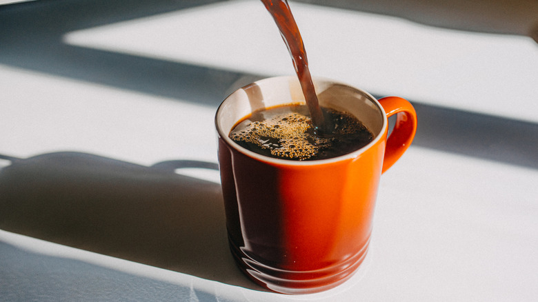 Coffee being poured into bright orange cup on table