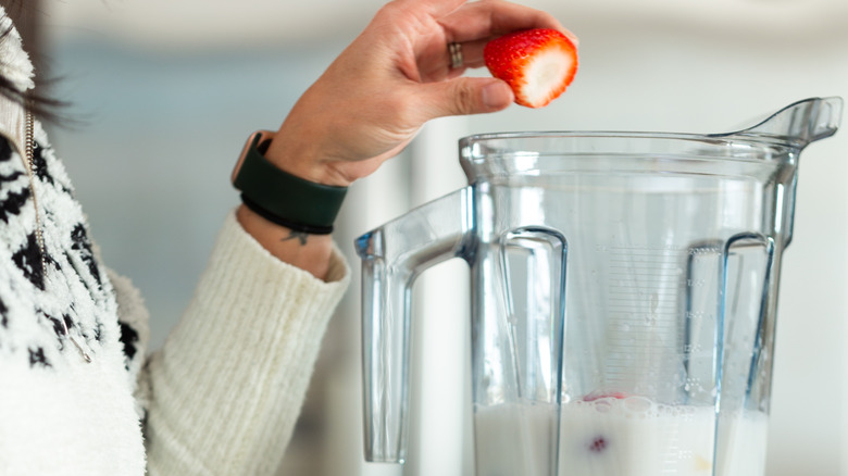 woman putting strawberry in blender