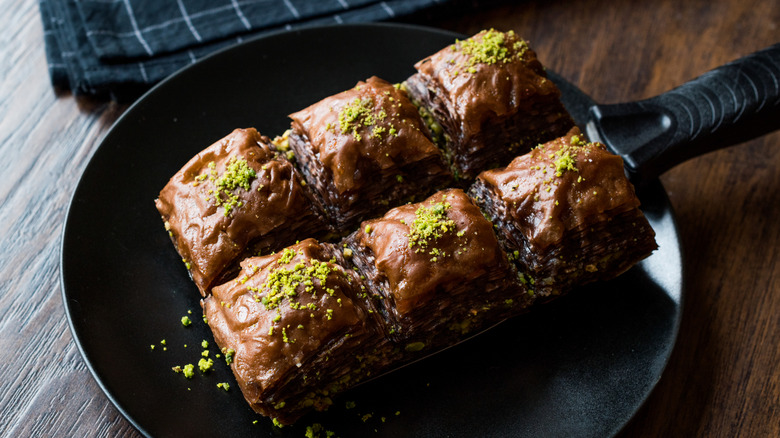 Chocolate baklava with crushed pistachio on black serving tray