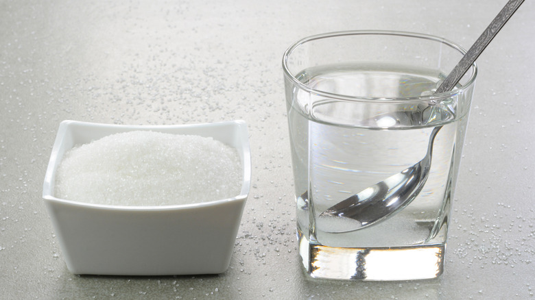 Cup of water and sugar in bowl on table