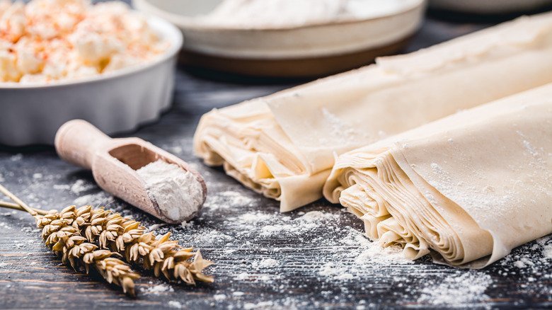 Sheets of phyllo dough on counter with scoop of flour