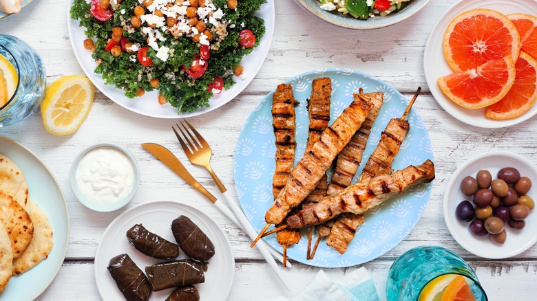 Grilled chicken skewers as part of a mezze spread plated on a blue dish surrounded by olives, stuffed vine leaves, salads, olives, and grapefruit
