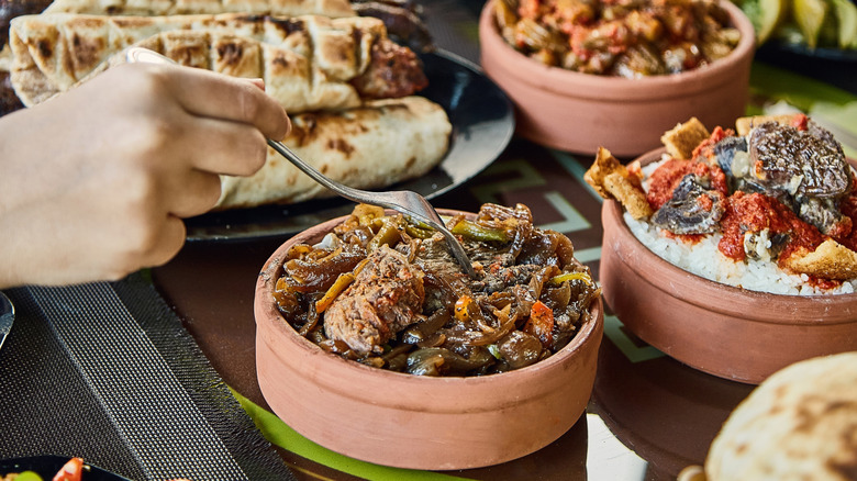 Several hands with forks reaching for mezze assembled in clay dishes