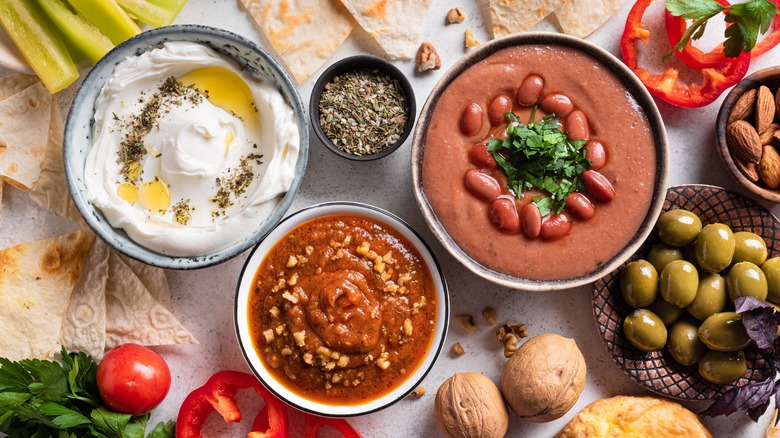 Top view of a table filled with a variety of colorful mezze dips, spices, olives, and nuts surrounded by fresh veggies and pita bread