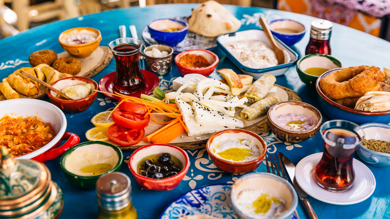 A mezze spread on a table with various bowls packed with dips and a central plate filled with fresh veggies and cheese