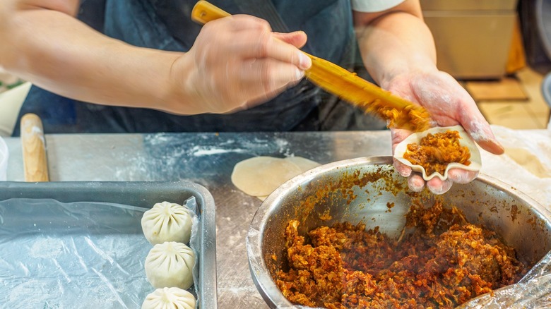 Hands filling a dumpling wrapper