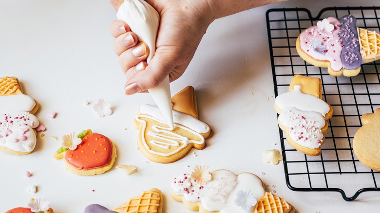 Person piping glaze onto cookies