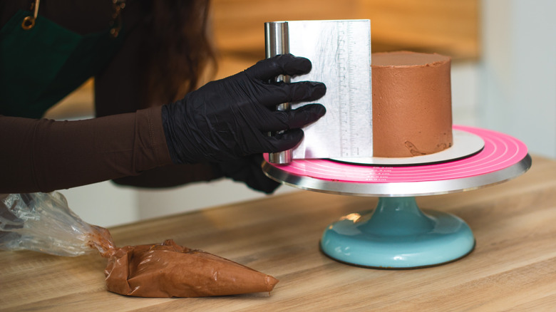 Using a bench scraper and turntable to smooth out cake frosting