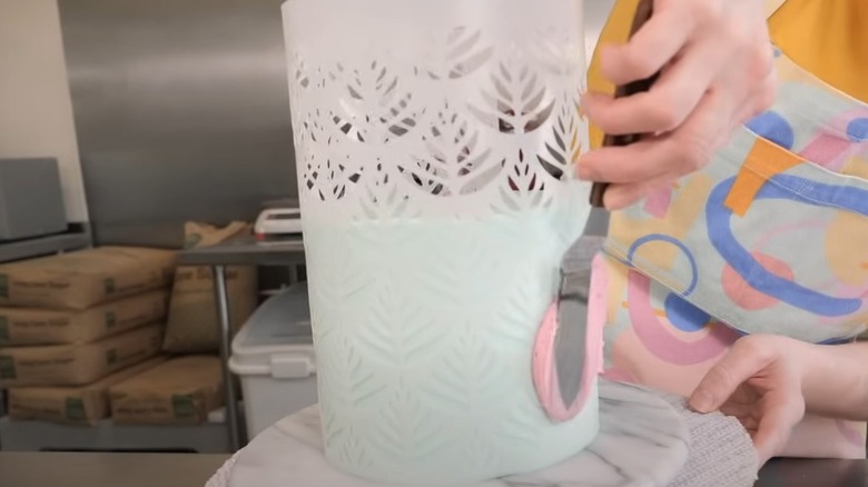 Applying stencil to frosted cake with pink frosting