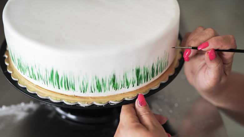 Painting a fondant-covered cake with a green pattern using a tiny brush