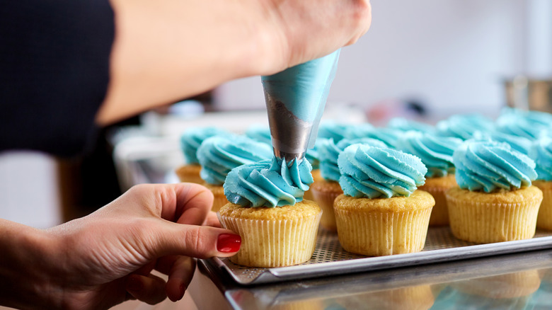 Piping blue frosting onto cupcakes