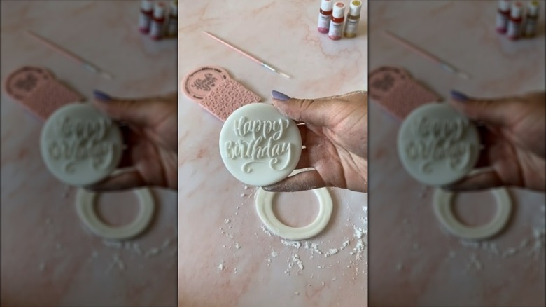 Hand holding circle of fondant icing with "Happy Birthday" stamped into it