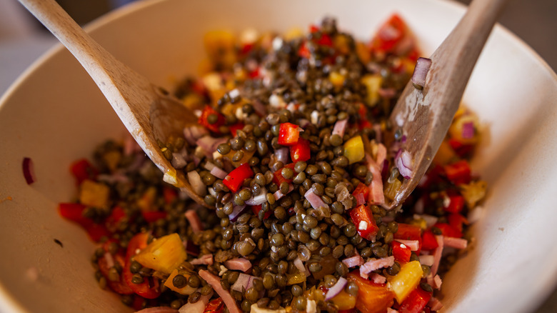 Green lentils with salad dressing in bowl with two spoons