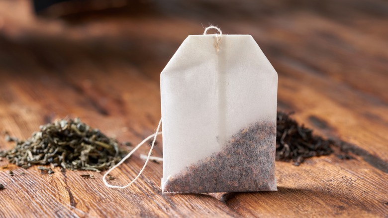 Chai tea bag sitting on a wooden table with heaps of loose tea in he back