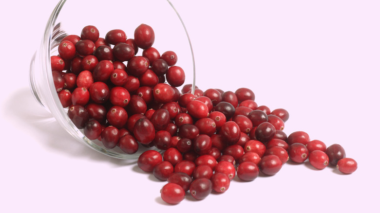 Fresh cranberries spilling out of clear bowl on a pink counter