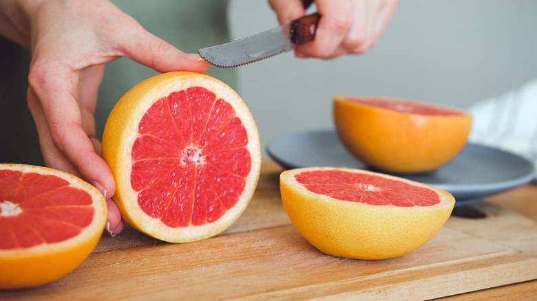 A person slicing grapefruit on a wooden cutting board surrounded by other grapefruits